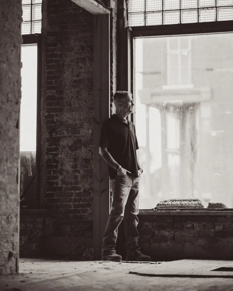 Jim Lunsford standing beside a tall window in a brick interior.
